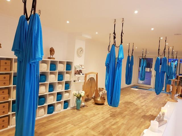 Ein Raum mit Aerial-Yoga-Tüchern und Meditationskissen in einem Regal